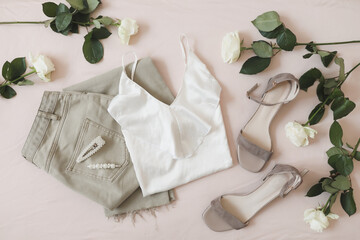 Overhead view of woman's casual spring summer outfit. Jeans, sandals, accessories and flowers on beige background. Flat lay, top view.