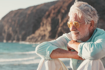 Beautiful bearded senior man sitting on the beach looking at horizon and sunset light