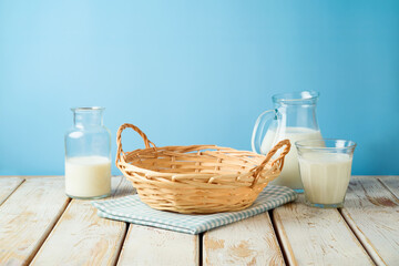 Empty wicker basket with tablecloth and milk bottles on rustic table over blue wall  background.  Kitchen mock up for design and product display.