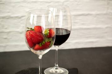 Ripe juicy red beautiful strawberry close-up is an appetizing fresh snack paired with glass of red wine