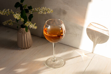 glass of rose wine in sun light, shadow, bird cherry flowers in vase on white backgroun