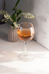 glass of rose wine in sun light, shadow, bird cherry flowers in vase on white backgroun