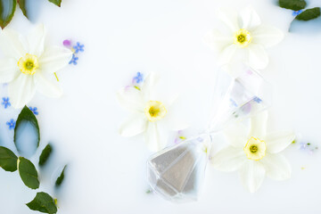Creative floral background.Hourglass,daffodil and forget-me-not flowers floating in milk.Top view,selective focus.