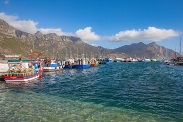 Fototapeta premium panaramic view on Hout Bay, the southern Harbor of Cape Town, with characteristic table cloth clouds rolling over the mountains,South Africa, landscape 