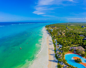Aerial view of palms on the sandy beach of Indian Ocean at sunny day. Summer holiday in Zanzibar, Africa. Tropical landscape with palm trees, white sand, blue water, hotels. Top view of sea coast