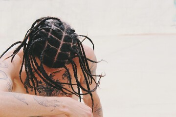 Portrait of young man shirtless with tattoos on skin and tight hair braids , hairstyle / style 