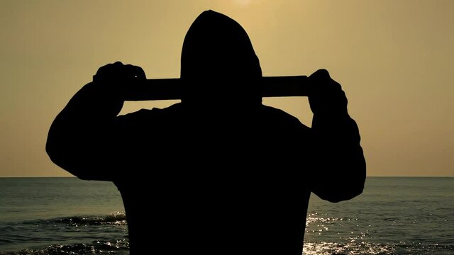 The black silhouette of a man in a hoodie, over a beautiful sunset at sea, unrolling adhesive tape, sealing the viewer's mouth or eyes. Symbolic shot: repression, censoring, silencing.
