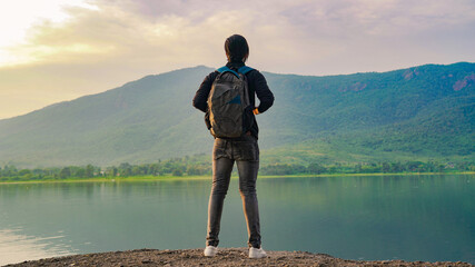 Young man standing near the lake and mountain and enjoying the view of nature