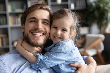 Close up portrait of smiling little girl child hug cuddle excited young Caucasian father show love care. Happy small preschooler kid daughter embrace dad feel grateful thankful. Fatherhood concept.