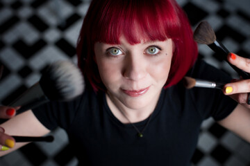 red-haired young woman showing her makeup brushes