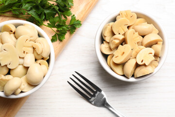 Delicious marinated mushrooms in bowls on white wooden table, flat lay