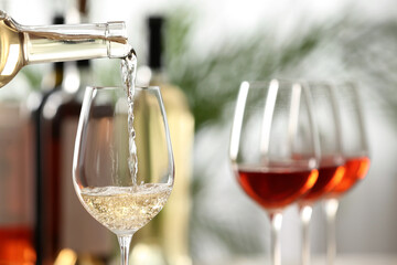 Pouring white wine from bottle into glass on blurred background, closeup. Space for text