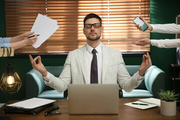 Calm businessman meditating at office desk in middle of busy work day