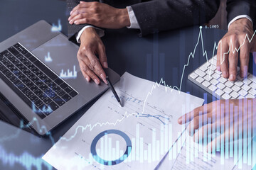Two traders man and woman researching historic data to predict stock market behavior. Internet trading concept. Forex and financial hologram chart over the table with the documents
