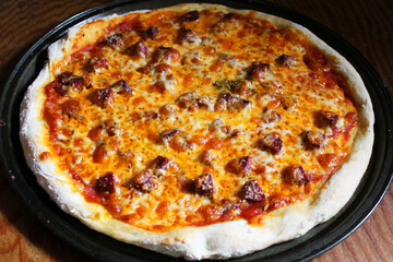 Close-up of fresh baked, homemade pizza, still on pan, on wooden cutting board.
