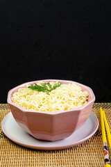 Quick instant noodles with parsley in a pink bowl on  grey tablecloth, Asian Chinese ramen pasta fast food eaten with yellow bamboo chopsticks