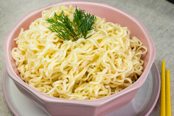 Quick instant noodles with parsley in a pink bowl on  grey tablecloth, Asian Chinese ramen pasta fast food eaten with yellow bamboo chopsticks