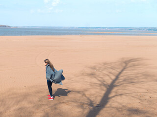 girl with long hair walking on river coast at sunny day, tree shadows on sand