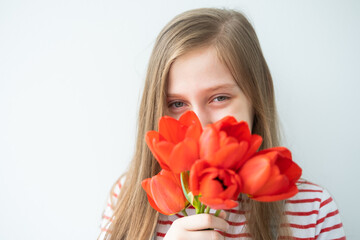 portrait happy teenage girl with long hair with red tulips standing against white wall