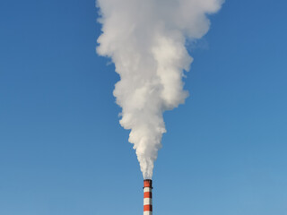 White smoke from a red and white chimney of a factory against a bright blue sky. Environmental pollution. Ecology and nature protection concept. 