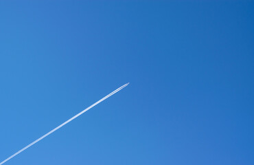 Travel, vacation concept. An airplane flying high, leaving a white trail against a blue sky. Place for your text.  Horizontal photo.	
