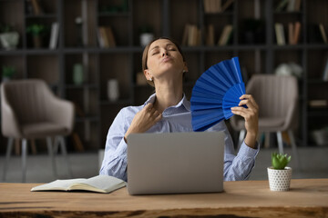 Too warm indoors. Sweaty young woman employee sit by laptop at uncomfortable hot office try to...