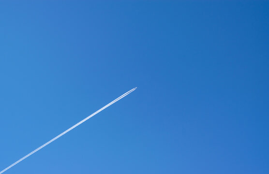 Travel, vacation concept. An airplane flying high, leaving a white trail against a blue sky. Place for your text.  Horizontal photo.	

