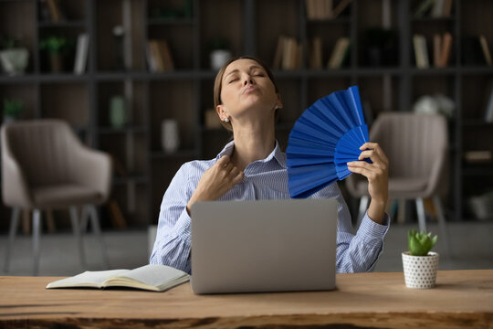 Too Warm Indoors. Sweaty Young Woman Employee Sit By Laptop At Uncomfortable Hot Office Try To Avoid Overheating Use Paper Fan. Sad Teen Female Tired Of Work In Unventilated Room Breath Hard Need Ac