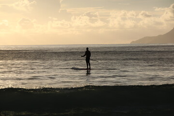 Silhouette of a man with a paddle on a board in the sea doing sports at dawn.Stand up paddle surfing.The concept of recreation and active lifestyle