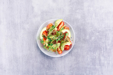 Salad with tomatoes, ovacado and micro greens on a gray table