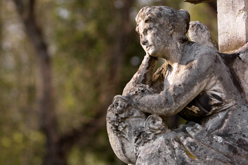 Beautiful sculpture of a seated angel with an illuminated face. Blurred trees in the background.