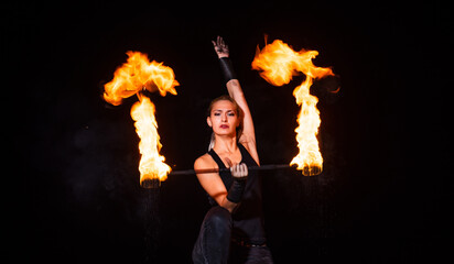 Sexy girl artist twirl burning batons during sparkling fire performance in darkness, lighting