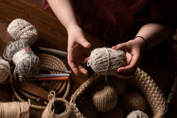 hands of craftwoman with a ball of jute yarn, tool for crochertting on table