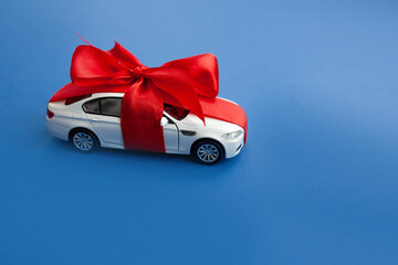 
white car with gift red ribbon with bow isolated on blue background. copy space