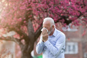 Man with allergy symptoms sneezing outside in springtime