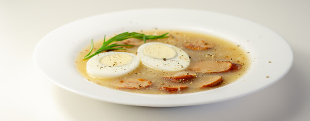 Traditional polish sour soup with sausage and eggs in a white deep plate