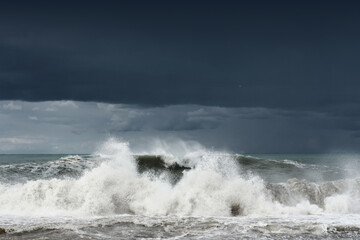 View of a stormy sea and dark cloudy dramatic sky, big waves are crashing on the shore