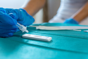 Female health care worker wearing blue surgical gloves and placing the sample in the covid-19 antigen diagnostic drug on a green surgical fabric 
