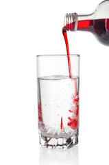 Cranberry and black currant syrup pouring into water glass on white background