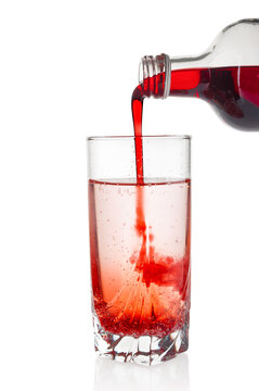 Cranberry and black currant syrup pouring into water glass on white background