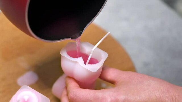 A woman occupied with hand made candles production, pouring melted wax into the mold. Slow motion