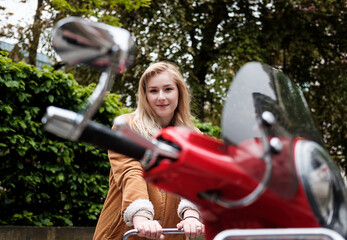 Naklejka premium Young blonde woman posing leaning on a red scooter.