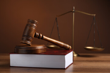 Judge's gavel with sound block, scales of justice and book on wooden table against brown background