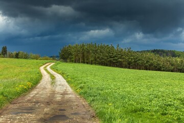 Fototapeta na wymiar Road to the storm. Dark storm clouds and dirt road in Czech Republic. Spring stormy weather in the Czech countryside.