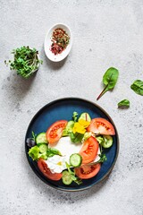 Appetizing salad with feta cheese, fresh vegetables (tomatoes, cucumbers, onions), crispy lettuce, microgreens and violet flowers. Non-standard serving of Greek salad.