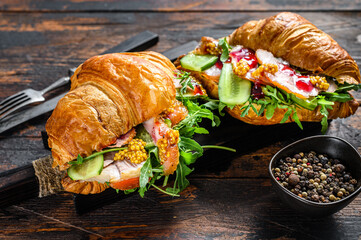 Croissant filled with ham and lettuce on wooden chopping board. Black background. Top view