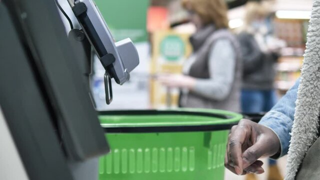 African man makes purchases at the self-service checkout in a supermarket, finger close-up, selects the desired goods on the touch screen goods against the background of shopping cart and other