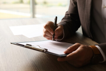 Businessman signing document at table indoors, closeup