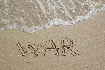 The word "war" on the sea sand, written with a finger with an oncoming sea wave and foam. A symbol stop the war