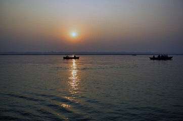 Varanasi, India: Wide angle Silhouette shot of People and tourists on wooden boat sightseeing in ganges river close to famous Munshi ghat during sunrise or sunset.